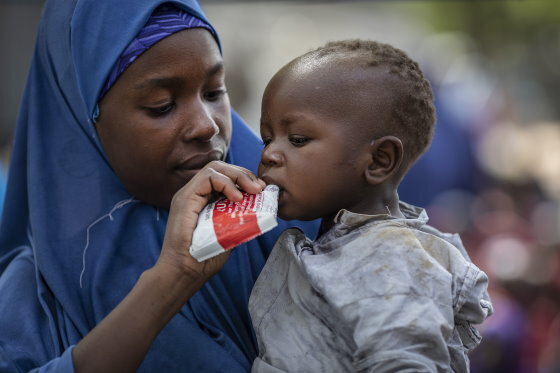 Photo: WFP/Siegfried-Modola、ボルノ州バマの国内避難民キャンプで、乳児のサディキ君（1歳）に重度の急性栄養不良治療用のピーナッツベースのペースト「Plumpy'Nut」を与えるアイシャさん（25歳）。