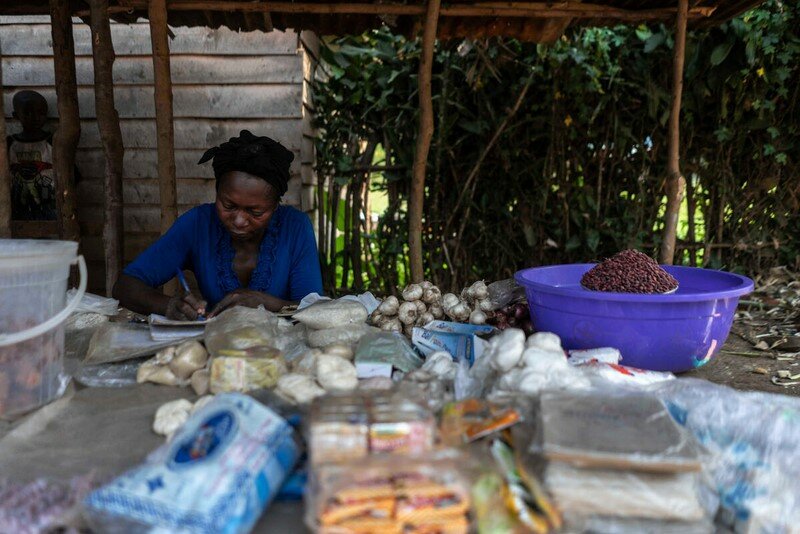 A woman writes in a book with produce around her.