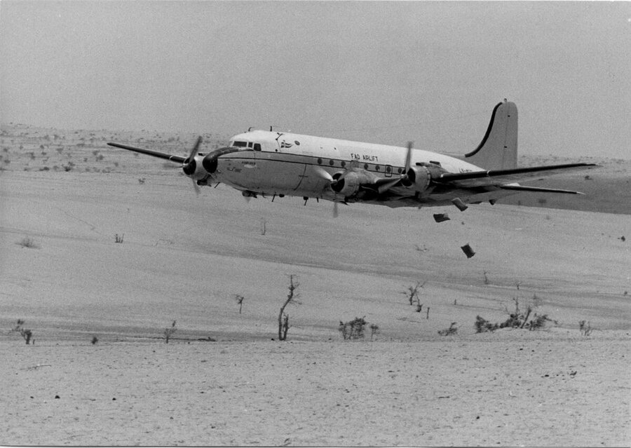b/w photo of aeroplane dropping food packages in the desert
