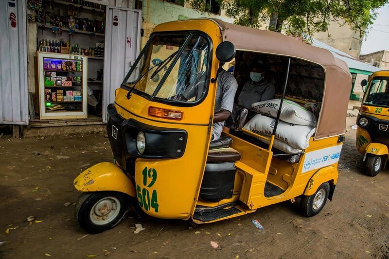 ナイジェリア北部の都市カノで、国連WFPのステッカーを貼ったケケ（3輪トラック）が食料を積んでコミュニティへ向かいます。