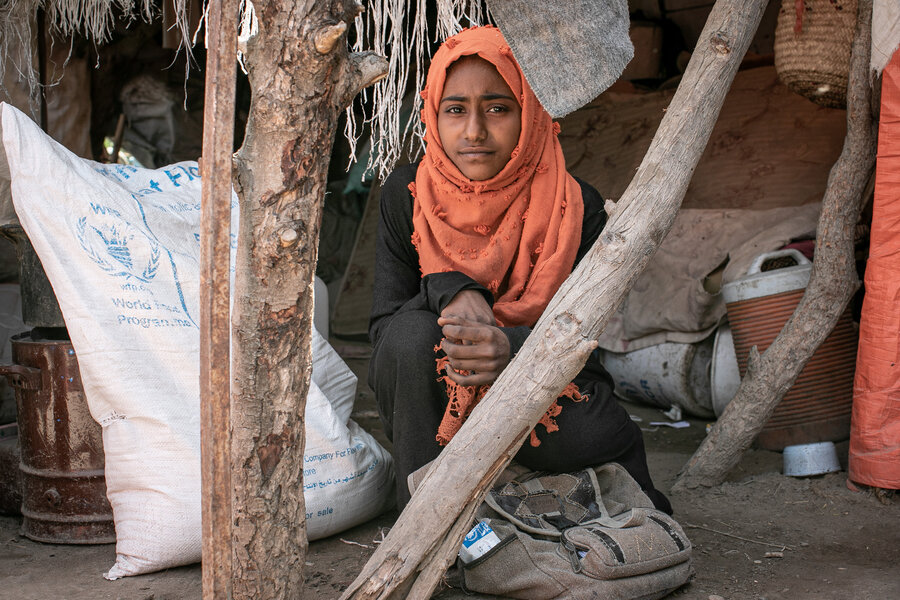 A girl in Yemen with a bag of WFP food assistance in the background