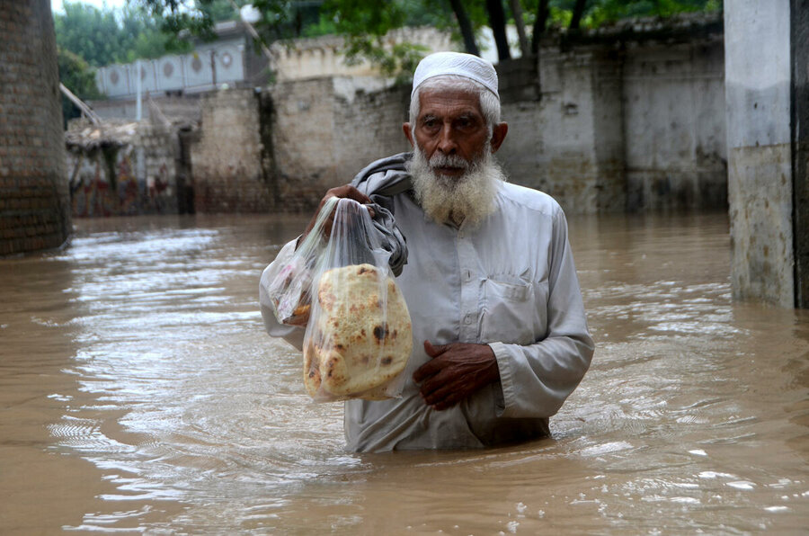 A man holds a bag of bread standing in a flooding street 