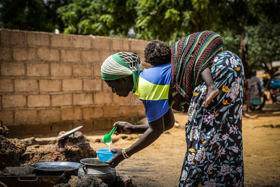 ブルキナファソのカヤで、生後10か月の子どもを抱いた母親が、国連WFPの支援プロジェクトで供与された栄養強化お粥をボウルに注いでいます。In Kaya, Burkina Faso, a mother carrying her 10-month-old child pours fortified porridge into a bowl, thanks to a WFP-supported project. Photo: WFP/Cheick Omar Bandaogo