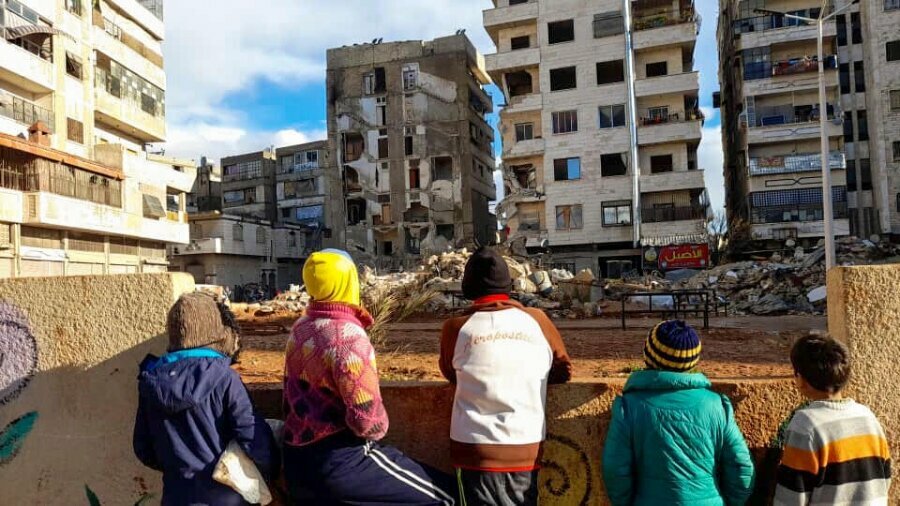 地震で破壊された建物を見つめるシリアのハマーの住民。