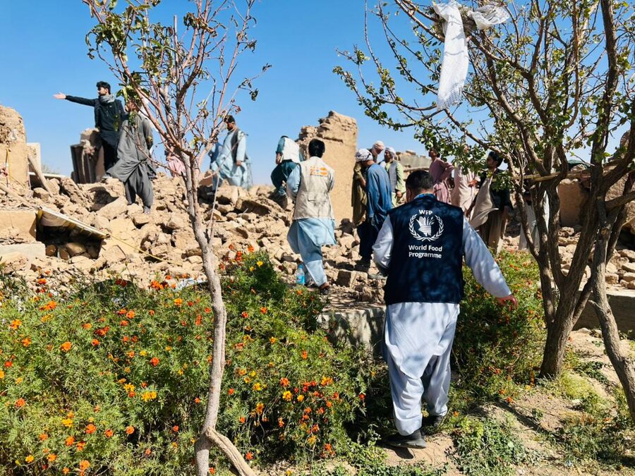 a man in salwar kameez and WFP vest walks toward a building destroyed by the earthquake in Afghanistan