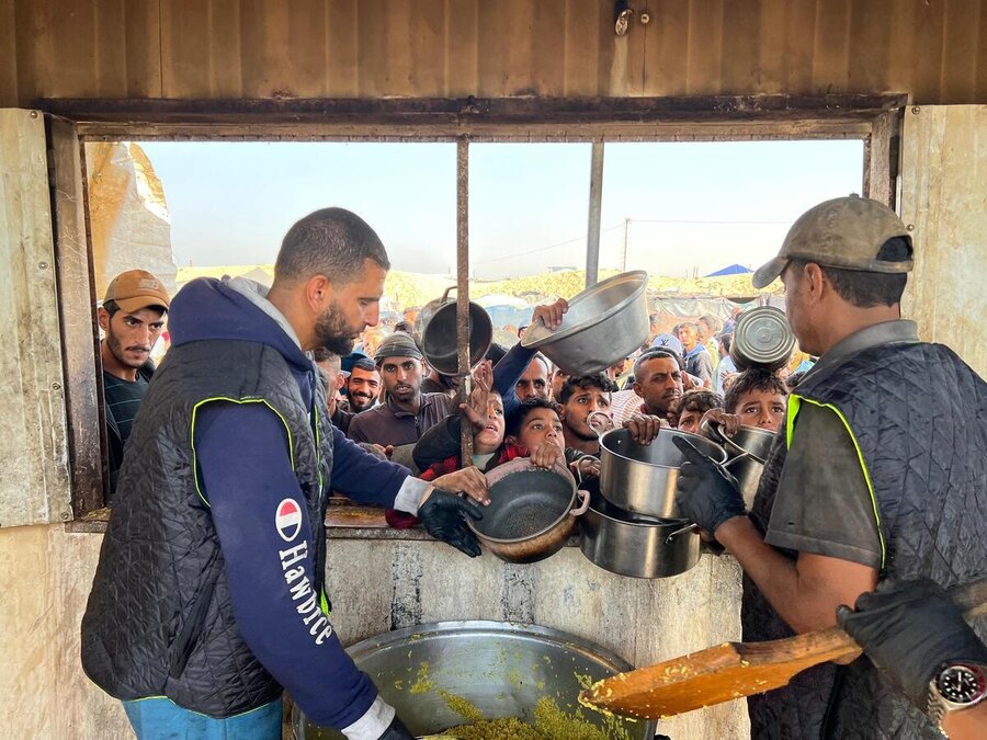 Two men dish out hot meals to children vying for pots to be filled