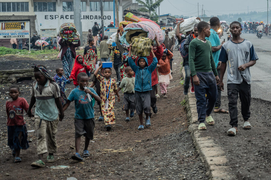 Displaced adults and children walk along the side of a road carrying belongings