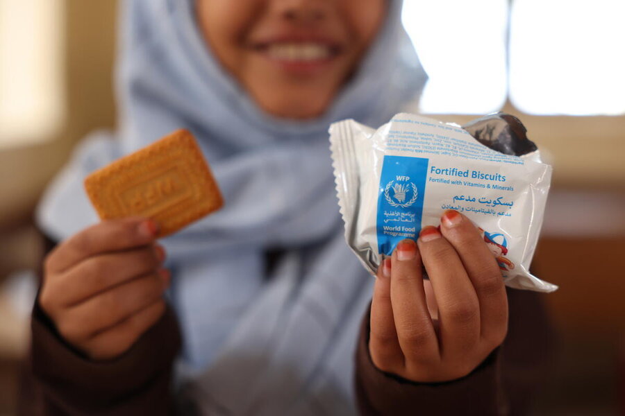 A biscuit along with its WFP wrapper in focus, held by a girl wearing a headscarf out of focus, and partially out of shot