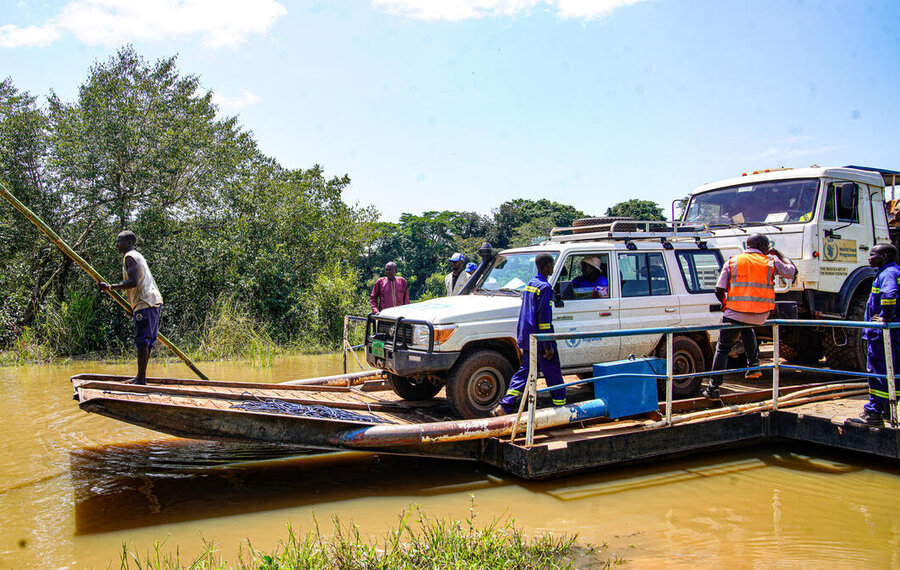A barge carrying a WFP vehicle and a truck is guided through brown waters by an oarsman