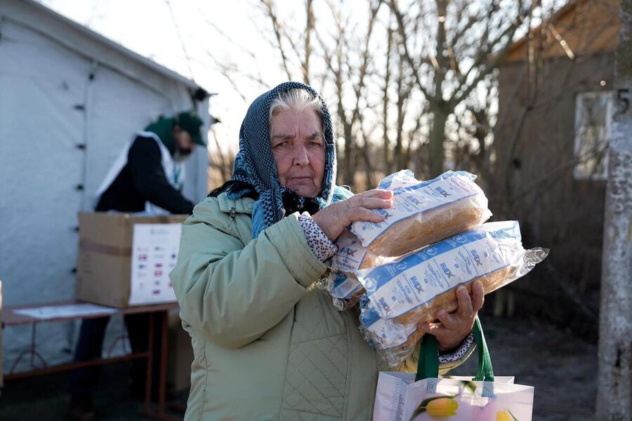 An older lady wearing a headscarf and a winter jacket carries loaves of WFP-branded bread