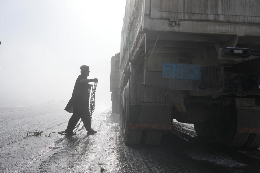 Silhoutted of a man carrying a chain as approaching the huge wheels of a WFP truck on the wet road - what's ahead is clouded by fog