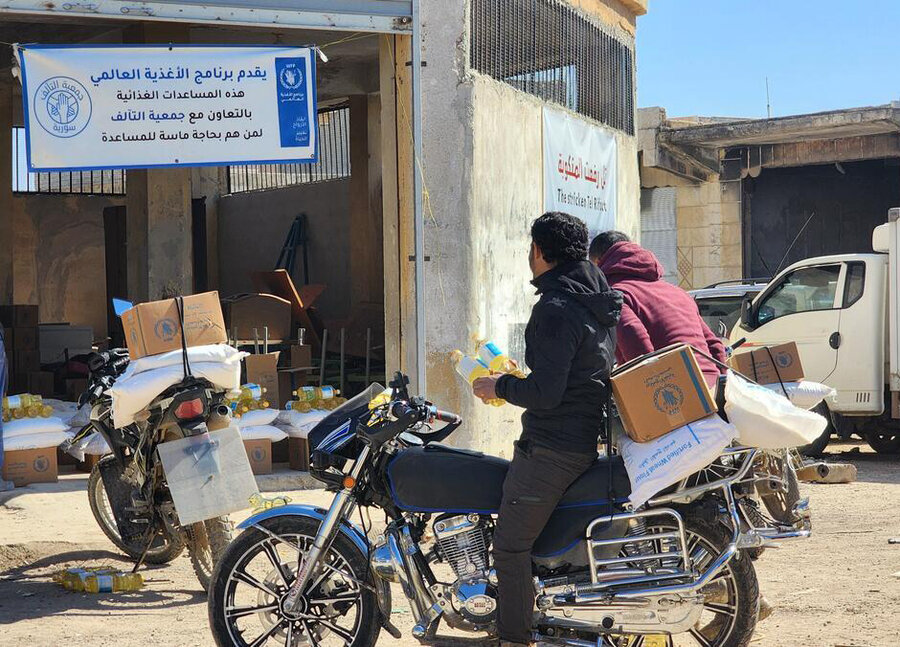 A couple arrives on a motorbike at a building where a WFP distribution banner hangs