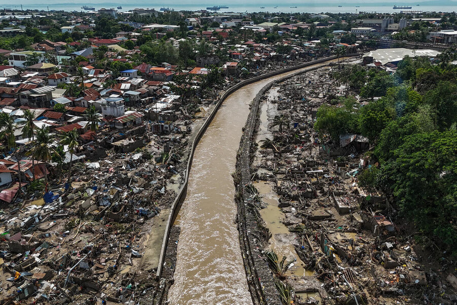 A muddied waterway snakes past rows of damaged homes, the sea visible in the background
