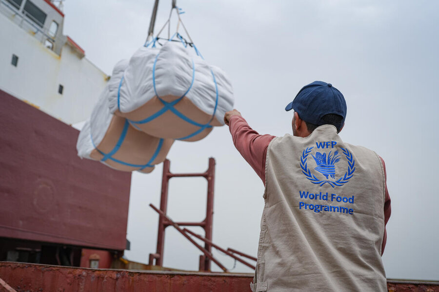 A WFP logistics worker guides cargo being lifted by crane onto a ship.