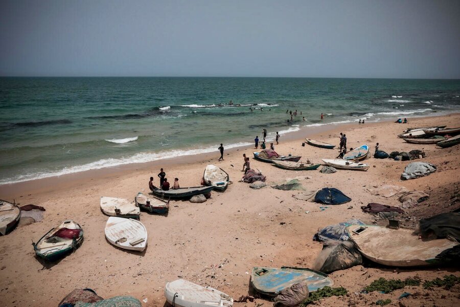 A wide view of a beach wth small wooden boats and people, with some also in the waves near the shore. Photo: WFP/Mohamed Hinnawi