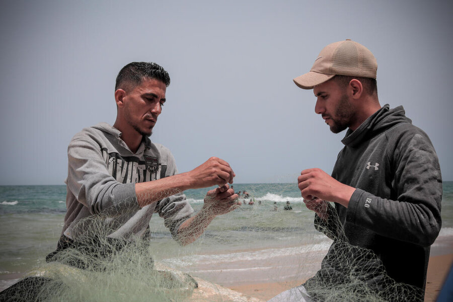 Two fishermen sit on a beach repairing a net. Photo: WFP/Mohammed Hinnawi 