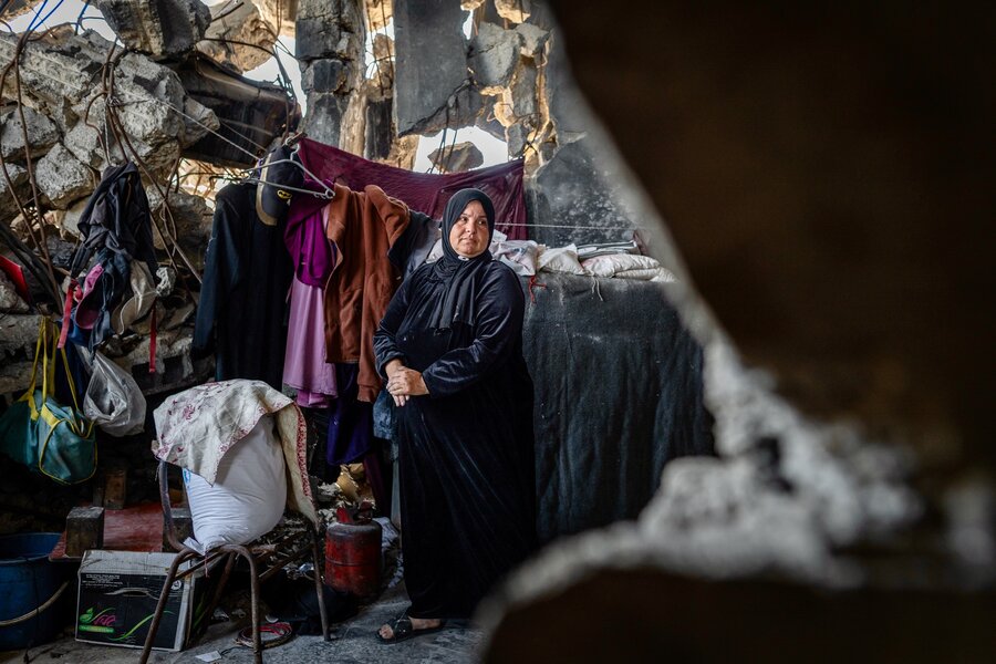 A woman in a black gown and headscarf stands in a heavily war-damaged building surrounded by clothes and other basic belongings. Photo: WFP/Maxime Le Lijour
