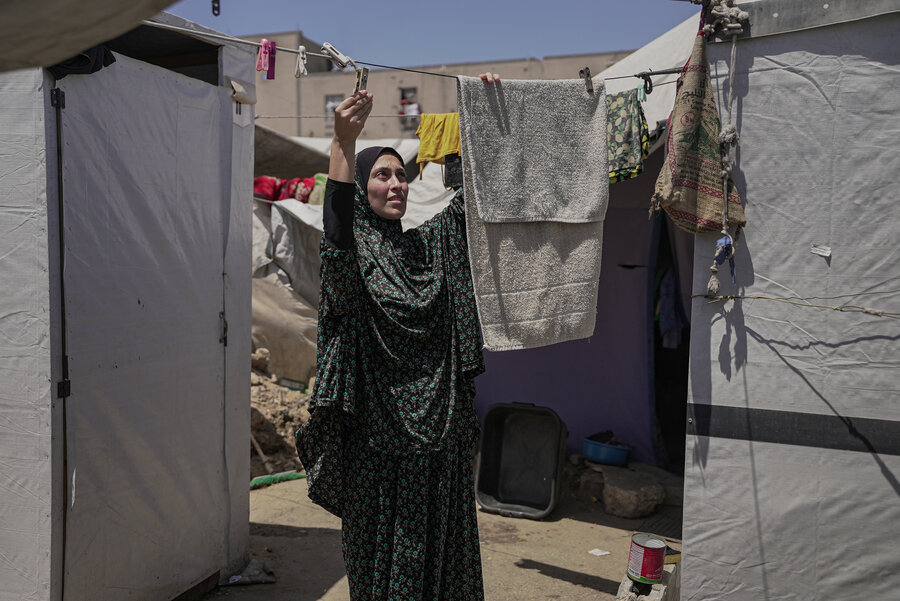 A woman wearing a headscarf hangs up towels on a line outside her tent in Gaza city. Photo: WFP/Jaber Badwan